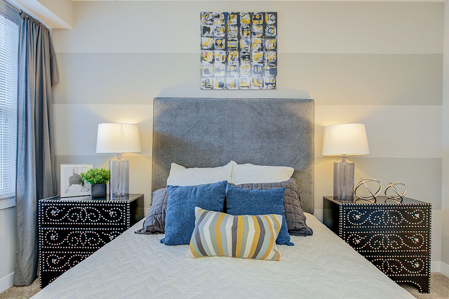 You can only use furniture and temporary decor to add personality. A gray bed with blue pillows and black side tables in a bedroom at Highpointe Apartments.