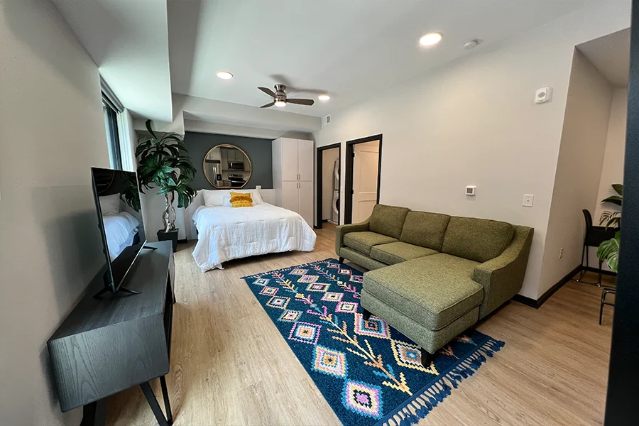 A large rug adds color to your apartment decor and visually creates a separate living space. A studio apartment showing a bed and a rug under a couch